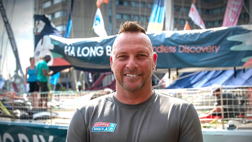 A man stands in front of sailing boats in a marina