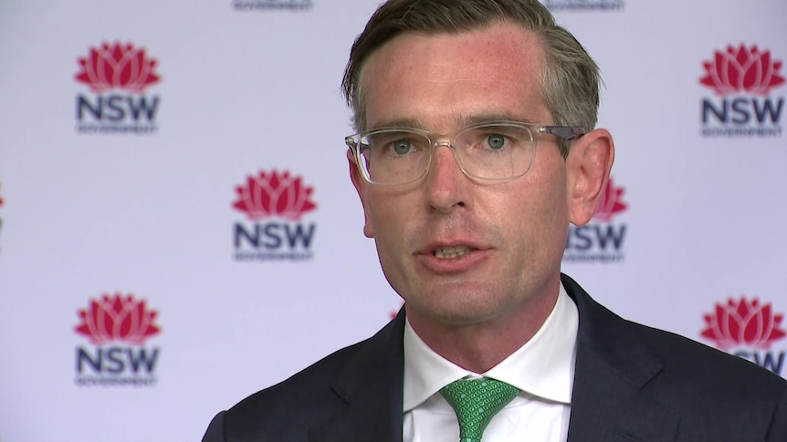 Closeup of suited man in glasses in front of NSW government branding. 