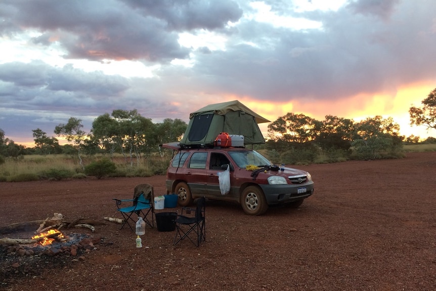 Mattis Mamczek's car with camping gear, a tent set up on the roof and an open fire burning while in outback Western Australia.