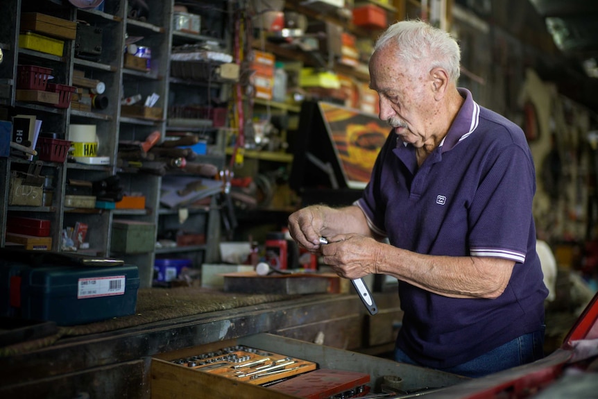 A man standing is an old car workshop getting ready to fix a car.