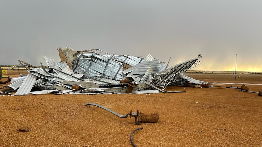 A large pile of metal sheeting on a red earth ground with dark storm clouds behind. 