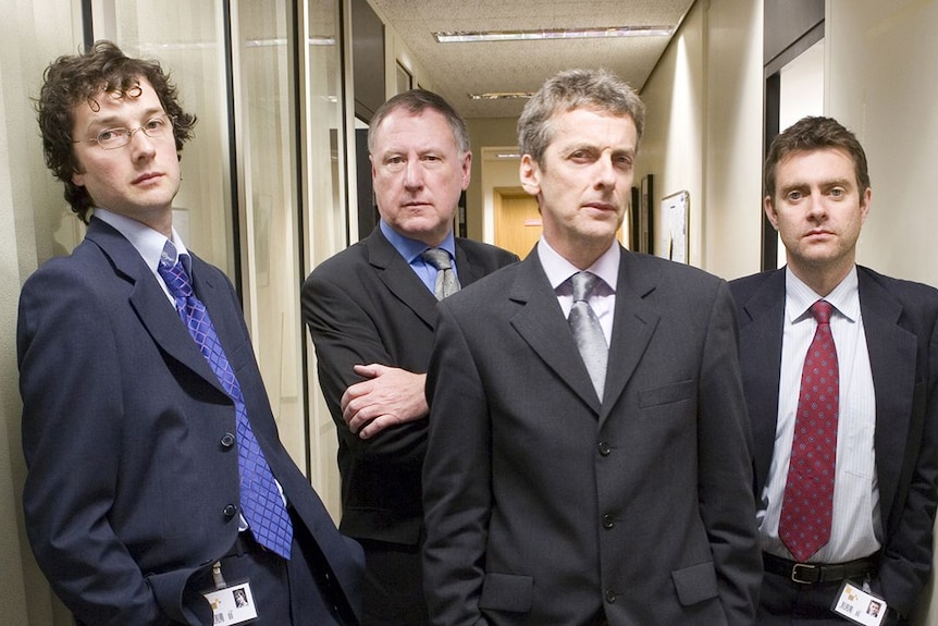 Four male actors in suits pose of a promo image in an office corridor