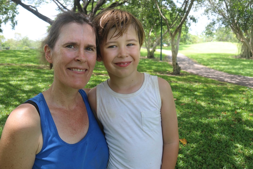 Karin Fullbrook and her son smile at the camera. They are in a lush green park and a path stretches behind them.