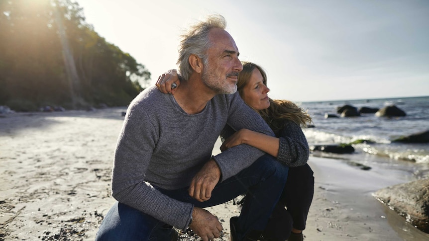 Mature couple crouching on the beach looking at view.