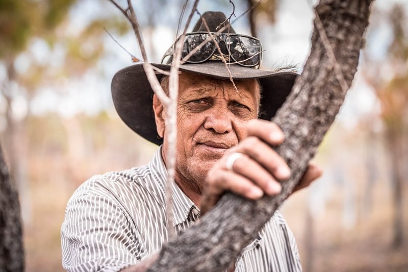 An older man wearing a cowboy hat, glasses on top, looking at the camera.