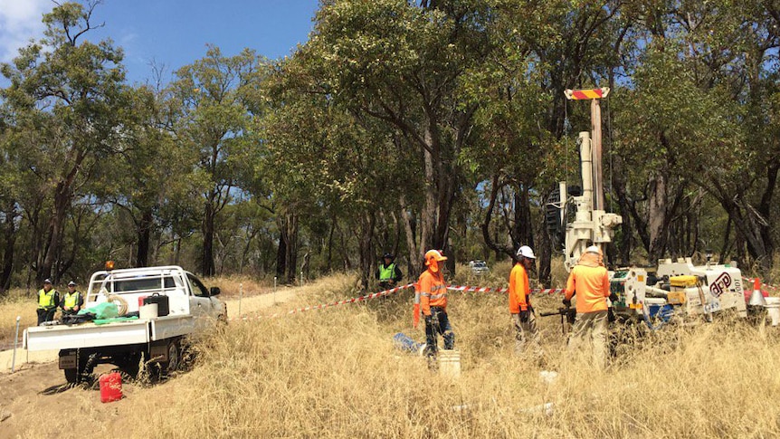 Workers stand around a drill rig in Bibra Lake, near a ute and two police officers.