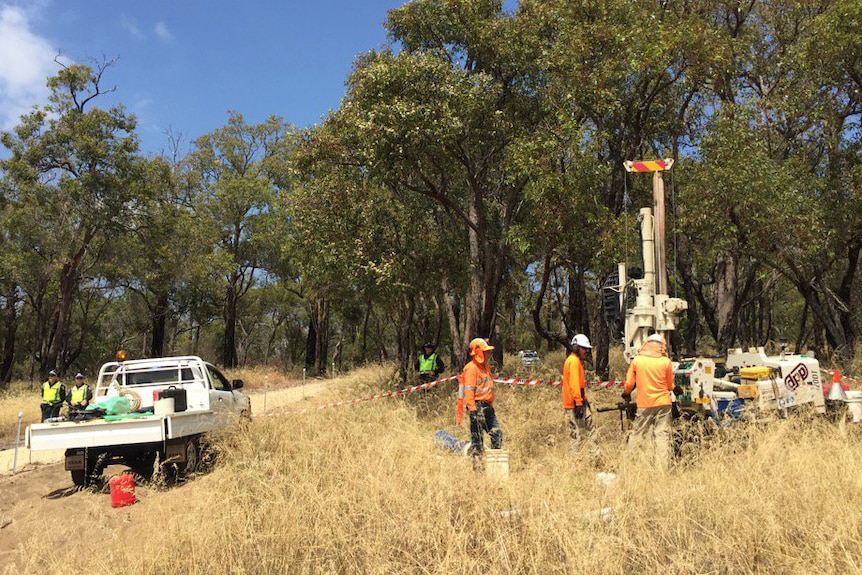 Workers stand around a drill rig in Bibra Lake, near a ute and two police officers.