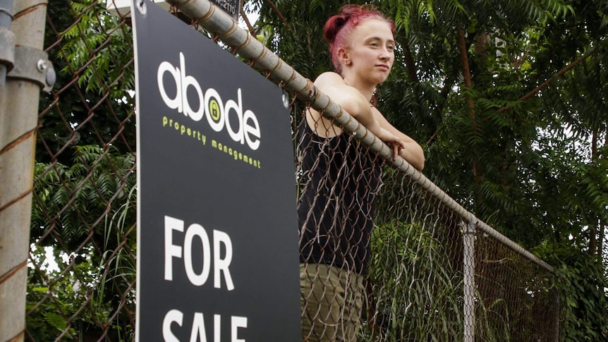 Palmerston mother-of-two Talitha Porter lanes against the fence of her front home, which has a 'For Sale' sign attached.