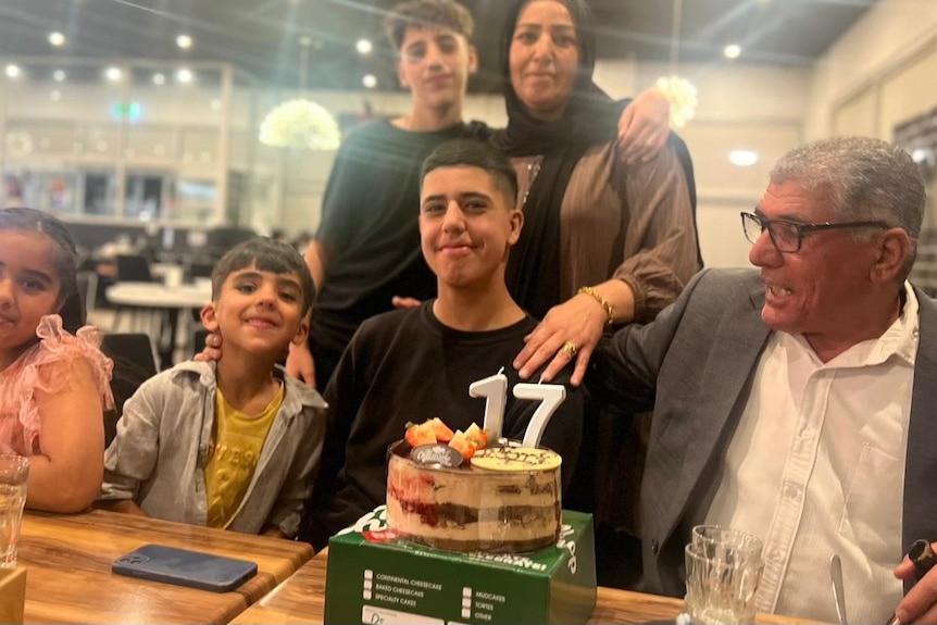 A family poses for a photograph at a 17th birthday party. Parents have their arms around their two sons, and two grandchildren