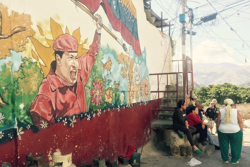 People sit in front of a mural of the late Hugo Chavez on the outskirts of Caracas, Venezuela.