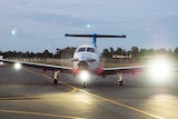A head-on shot of an RFDS plane on a runway with its lights on.