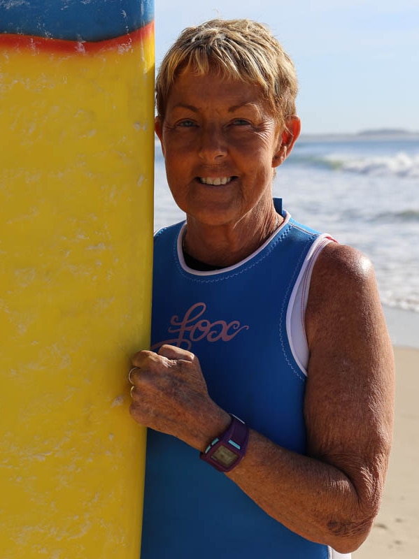 Robyn standing next to her surfboard on the beach.