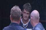 Brett Maston in a navy shirt, standing between two men with their faces turned.