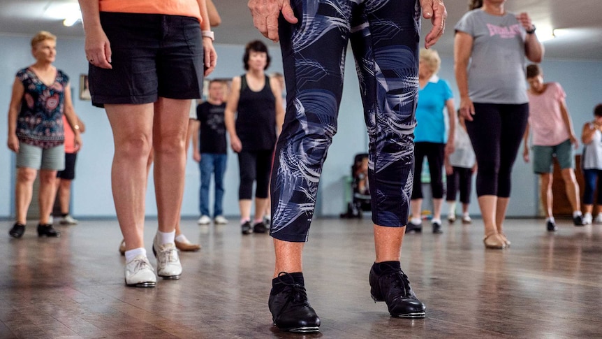 A group of people standing in a dance studio, with only the legs of the people in the foreground visible