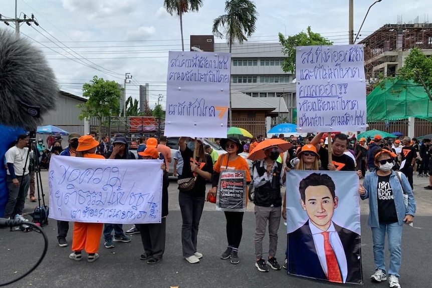 Protesters carry signs with Thai writing and a drawing of a young Thai pm candidate in a dark suit.