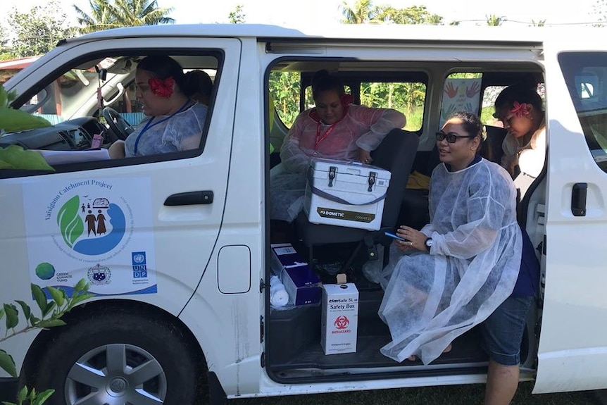 The side of a white van has its sliding door open as medical staff in protective clothing carry measles vaccines.
