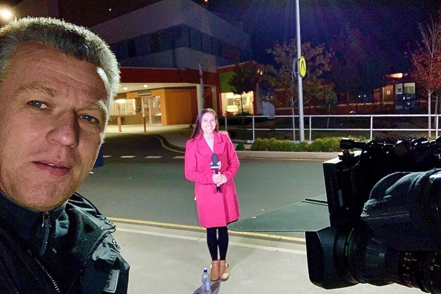Cameraman and journalist standing outside hospital at night.