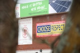 Two signs, including one that reads "choose respect",  hang on a red brick wall.