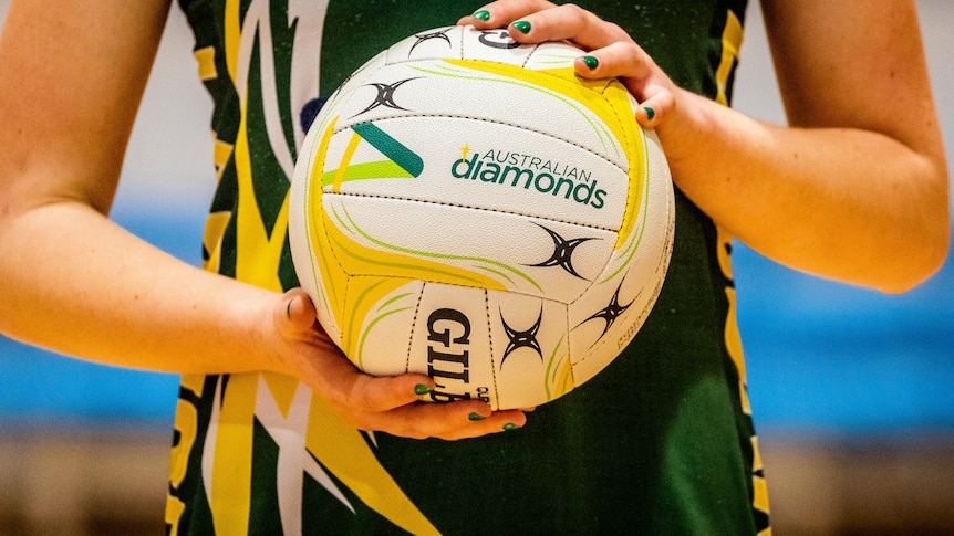 A green and gold dressed player holds a branded Australian Diamonds netball.