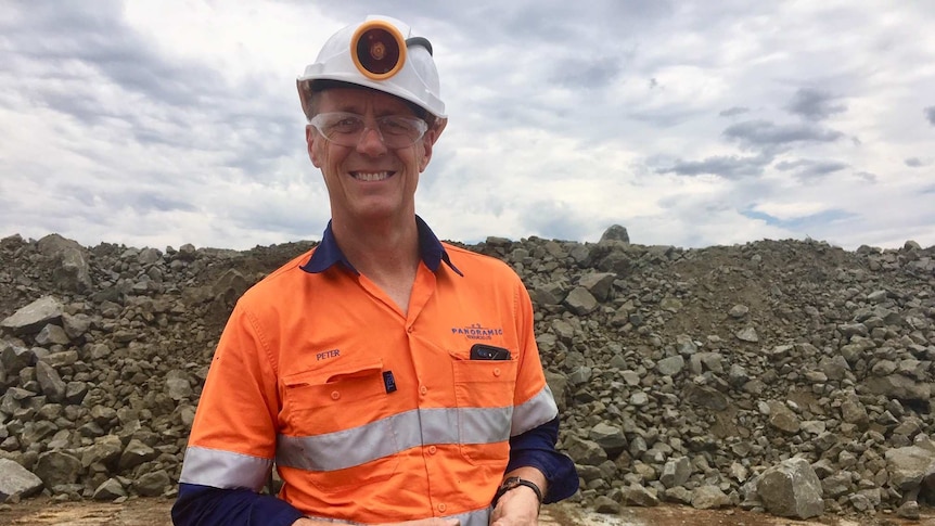 Man in high vis clothing and hard hat holding a lump of ore at nickel mine