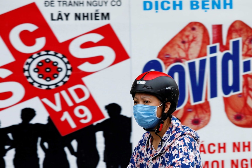 A woman wears a protective mask as she drives past a banner promoting prevention of COVID-19.