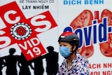 A woman wears a protective mask as she drives past a banner promoting prevention of COVID-19.