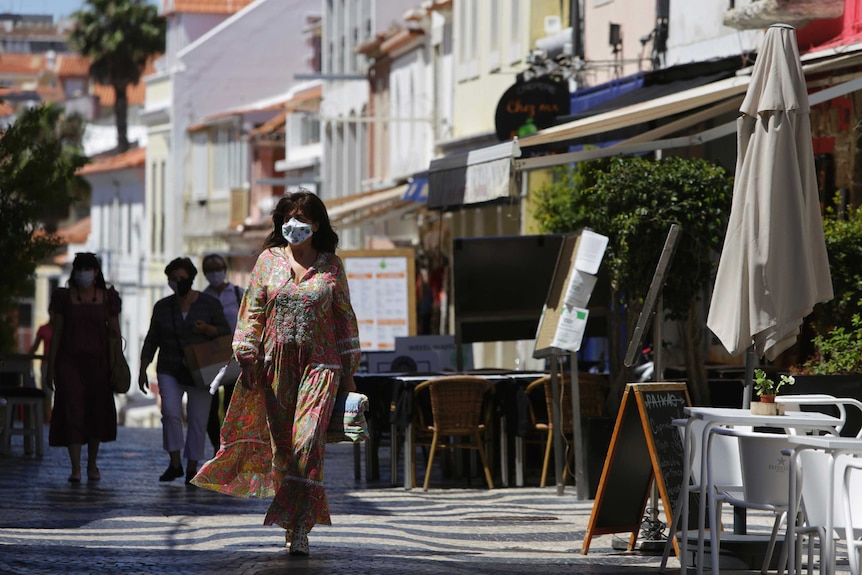 People wearing face masks walk past nearly empty restaurant terraces.