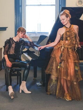 A teenage boy in black leather and sheer top at a grand piano, Nikki in a layered dress of sheer gold