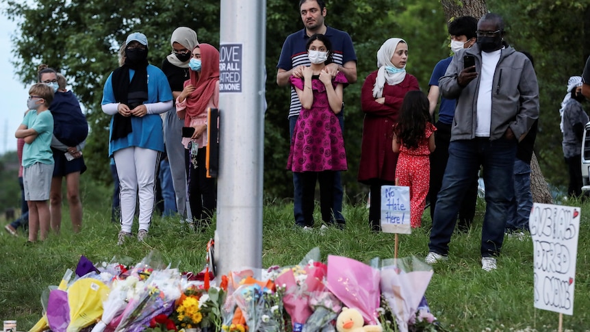 People gather at a makeshift memorial, covered in flowers, at the scene of the fatal crash. 