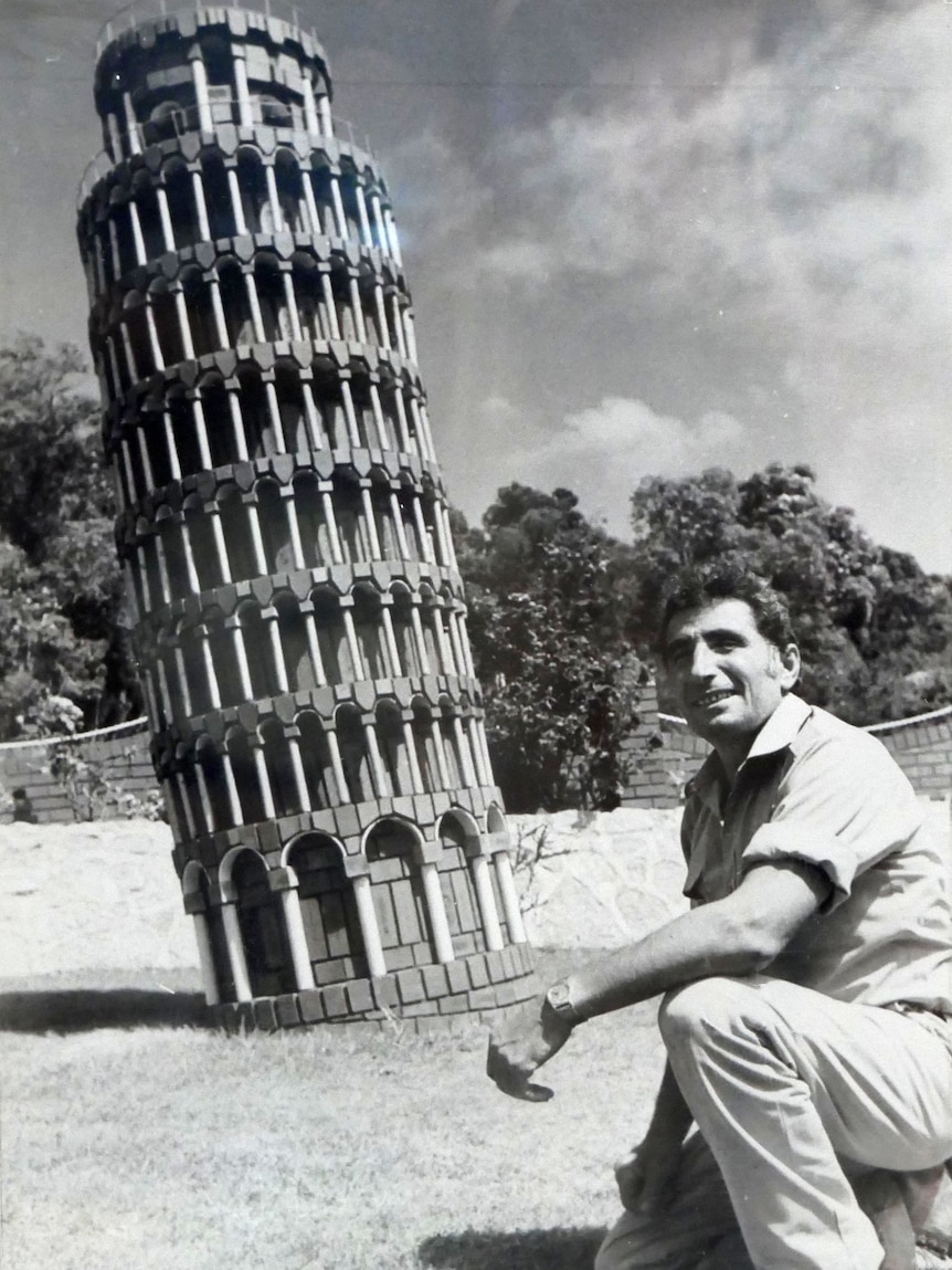A black and white photo of a man next to a replica of the Leaning Tower of Pisa.