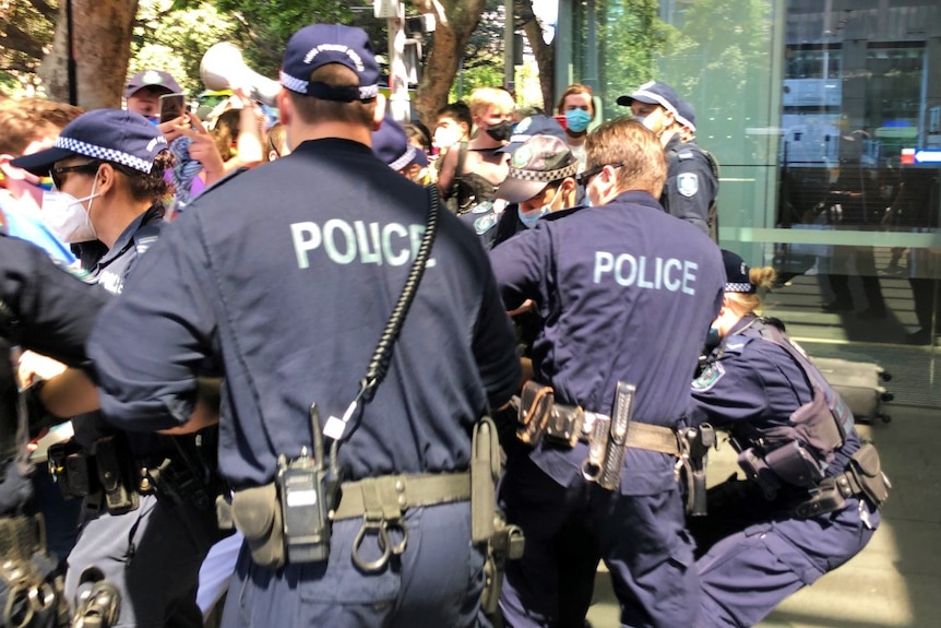 Several police in uniform in a group at a protest.