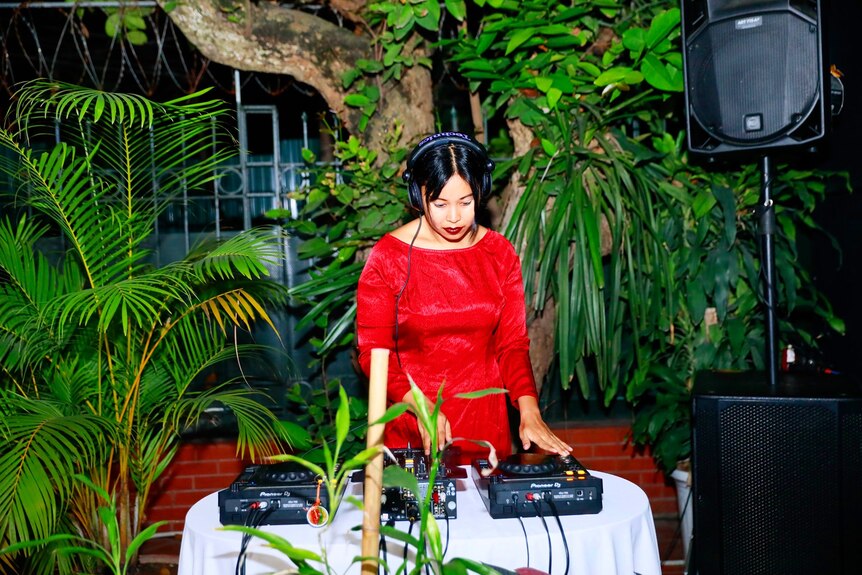 Maggie concentrates on her DJ decks in a red dress.
