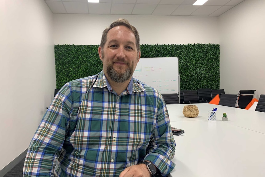 man in checked shirt and beard sitting at a white table in a  boardroom