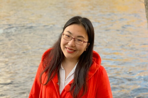 A woman standing besides a lake, smiling happily to the camera