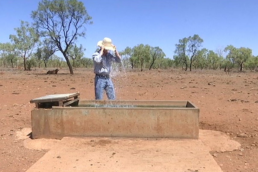 Farmer Luke Chaplain tips his hat full of water on his head from a water trough at Cloncurry.