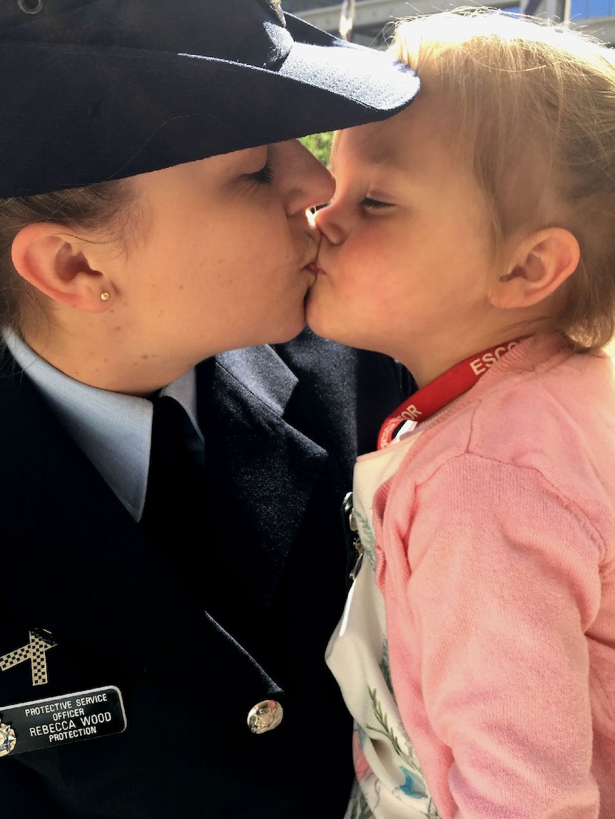 A woman in police uniform kisses a young girl.