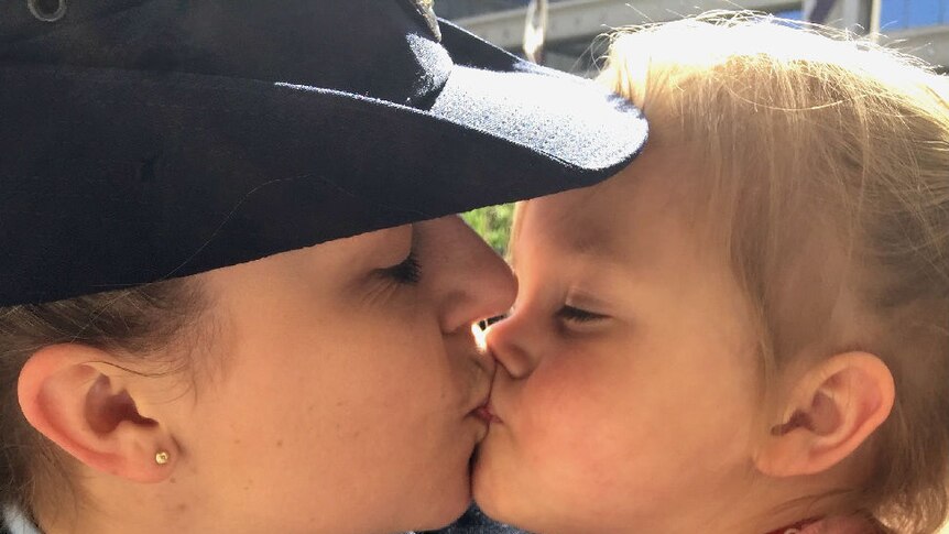 A woman in police uniform kisses a young girl.
