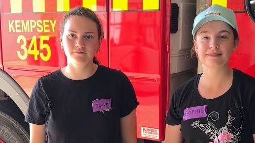 Two teenage girls in front of a fire truck close up wearing name tags 