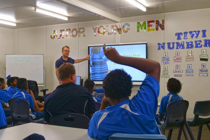 A presenter shows a popular meme to a class of students. Junior Young Men and Tiwi Numbers signs are posted up on the wall