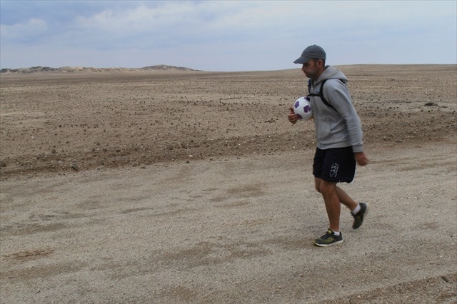 Matt Napier walking in the desert with a soccer ball under his arm.