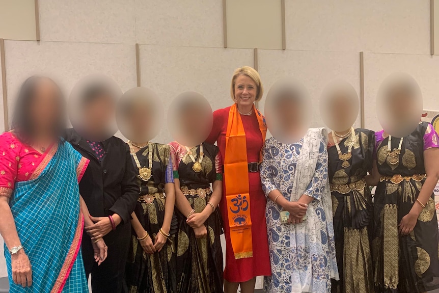 Kristina Keneally, wearing an orange scarf, poses for a photo with female dancers in traditional costume.