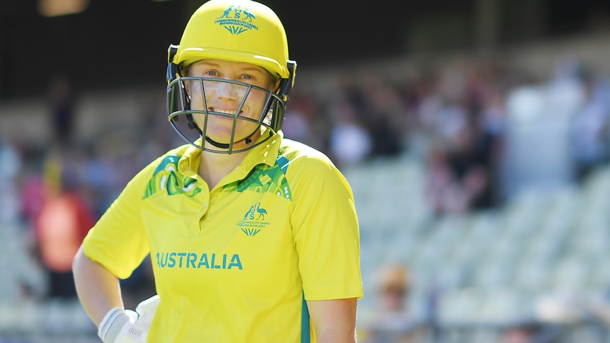 Alyssa Healy smiles while wearing yellow batting kit