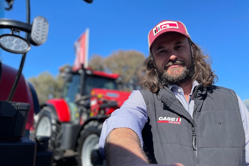 A man in a red cap stands in front of red tractors.