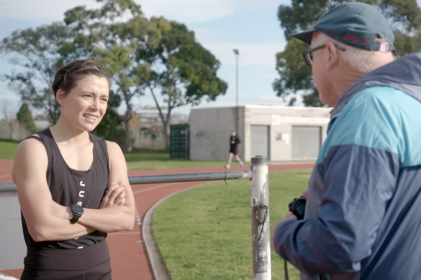 A runner stands with her arms folded while talking to her coach.