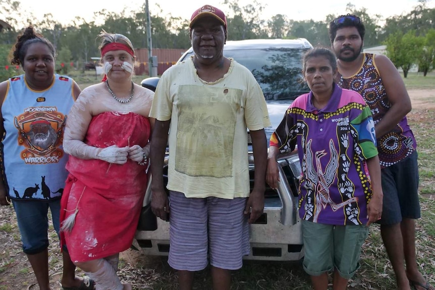 Five people stand in front a car and look at the camera