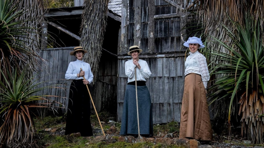 Three women in Edwardian dress posing in front of an old timber building.