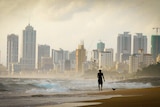 A man in silhouette walks along a beach in Sri Lanka with a series of high rises behind him 