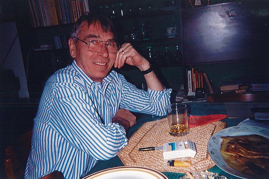 a man with glasses and a blue stripe shirt smiles at a table 