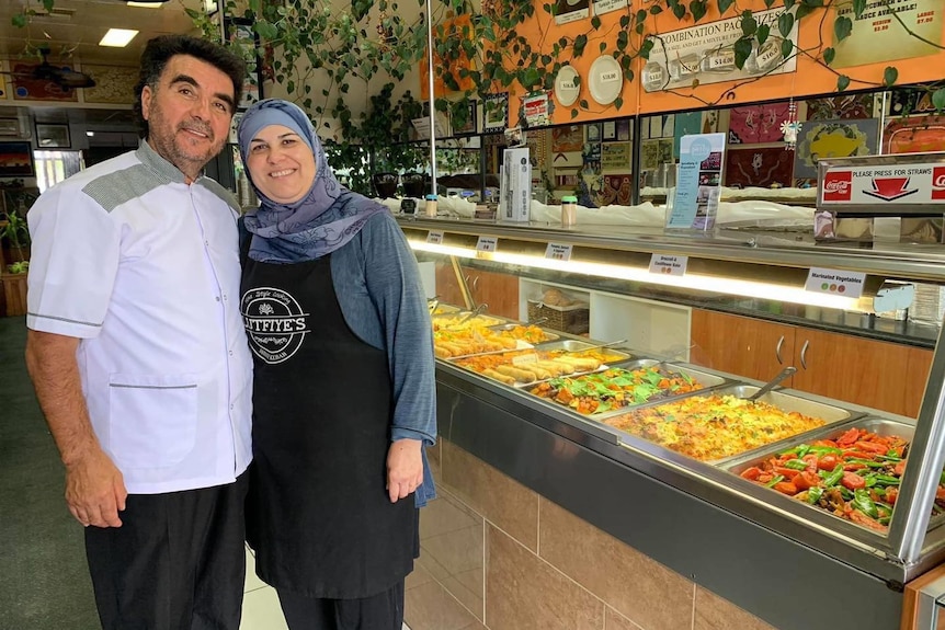 A man and woman standing in front of food display in a restaurant