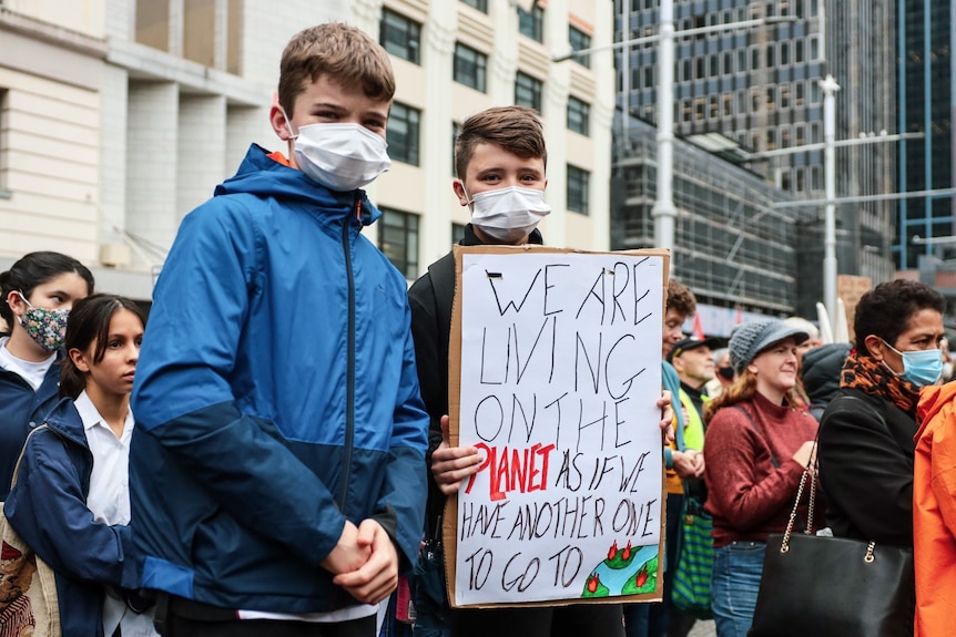 Two boys wearing face masks at a climate change rally, and one holds a sign.